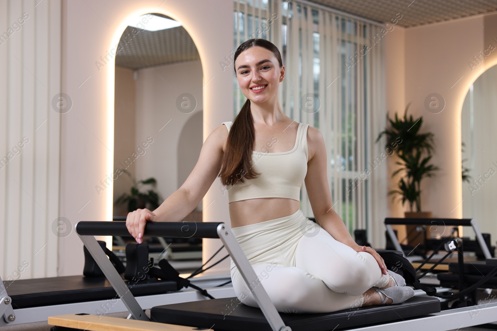 Woman sitting on reformer in pilates studio Photo of Woman sitting on reformer in pilates studio
