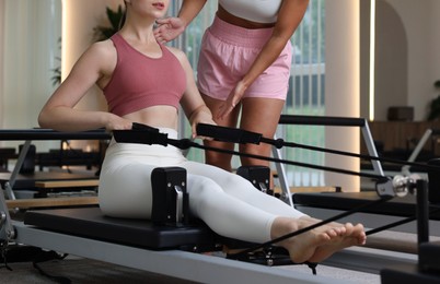Photo of Woman exercising on reformer supervised by pilates instructor in studio, closeup