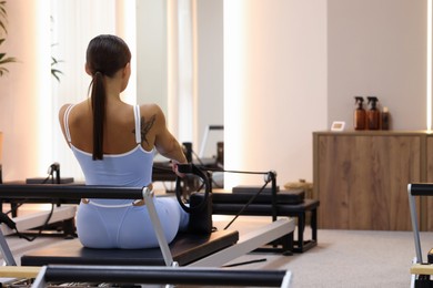 Photo of Woman exercising on reformer in pilates studio, back view. Space for text