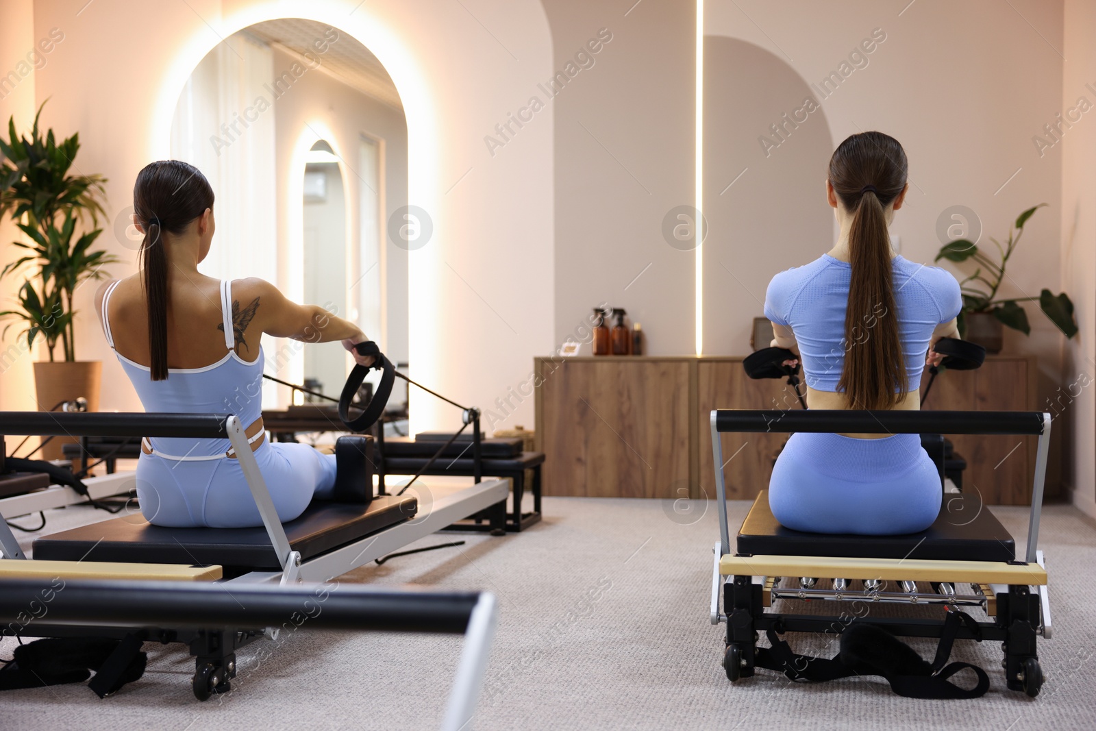 Woman and pilates instructor exercising on reformers in studio, back view Photo of Woman and pilates instructor exercising on reformers in studio, back view