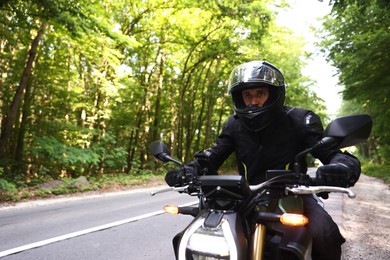 Photo of Young man in helmet driving modern motorcycle outdoors. Space for text