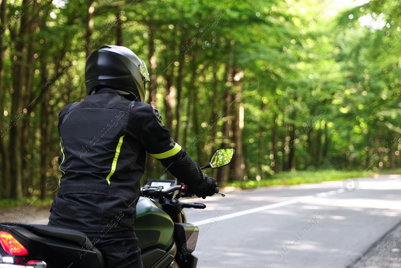 Young man in helmet driving modern motorcycle outdoors, back view. Space for text Photo of Young man in helmet driving modern motorcycle outdoors, back view. Space for text