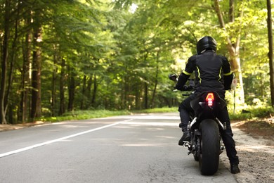 Photo of Young man in helmet driving modern motorcycle outdoors, back view. Space for text