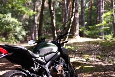 Photo of Modern black motorcycle parked in forest. Space for text