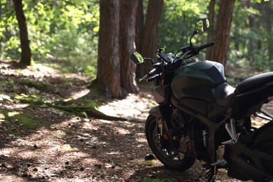 Photo of Modern black motorcycle parked in forest. Space for text