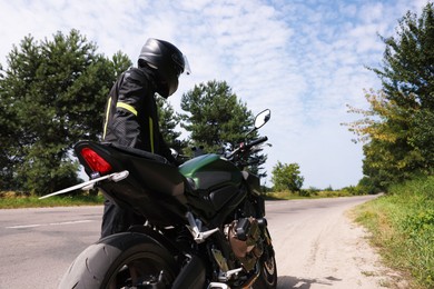 Photo of Young man in helmet with modern motorcycle outdoors, back view. Space for text