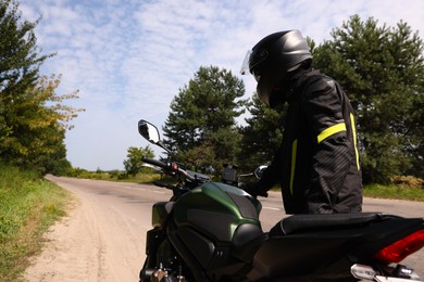 Photo of Young man in helmet with modern motorcycle outdoors, back view. Space for text