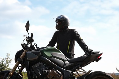 Photo of Young man in helmet with modern motorcycle outdoors