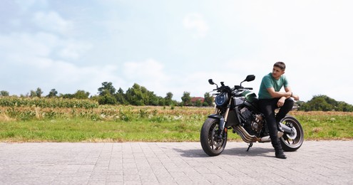 Photo of Handsome young man with modern motorcycle outdoors. Space for text