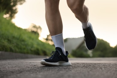 Photo of Athletic young man in sportswear running outdoors, closeup