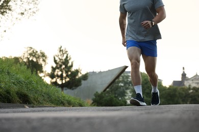 Photo of Athletic young man in sportswear running outdoors, closeup. Space for text