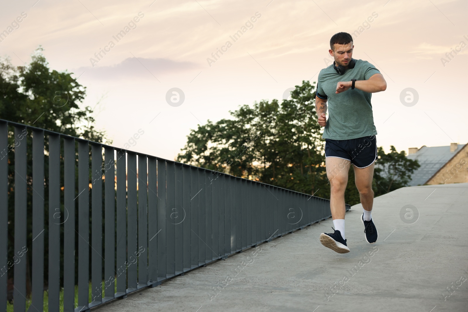 Athletic young man in sportswear running and checking fitness tracker outdoors, space for text Photo of Athletic young man in sportswear running and checking fitness tracker outdoors, space for text