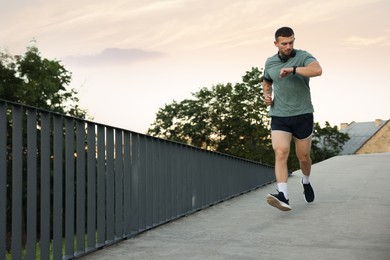 Photo of Athletic young man in sportswear running and checking fitness tracker outdoors, space for text