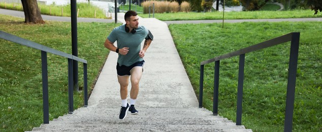 Photo of Athletic young man in sportswear running up stairs outdoors