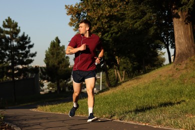 Photo of Athletic young man in sportswear running outdoors, space for text