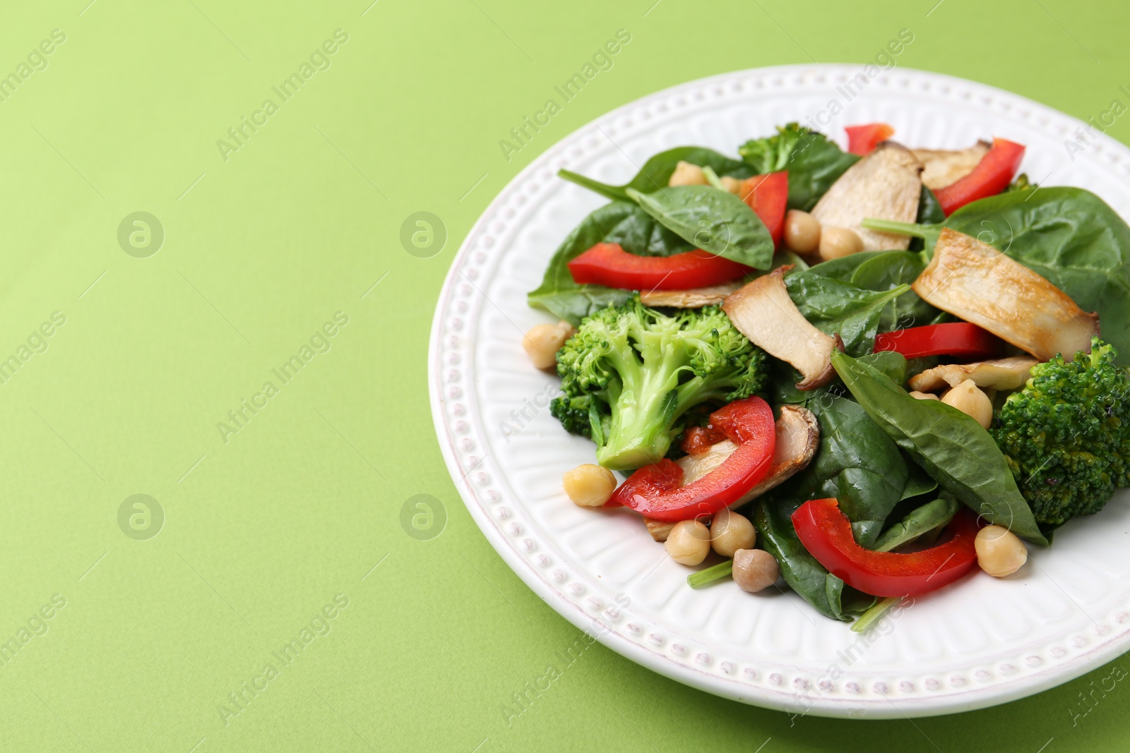 Tasty salad with eryngium mushrooms, chickpeas, vegetables and spinach on green background, closeup. Space for text Photo of Tasty salad with eryngium mushrooms, chickpeas, vegetables and spinach on green background, closeup. Space for text