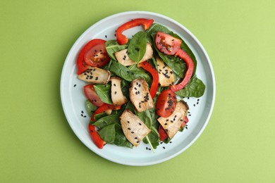 Photo of Tasty salad with eryngium mushrooms, vegetables, spinach and sesame on green background, top view