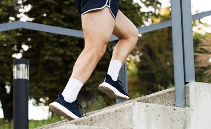 Photo of Athletic young man in sportswear running up stairs outdoors, closeup