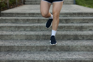 Photo of Athletic young man in sportswear running down stairs outdoors, closeup