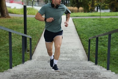 Photo of Athletic young man in sportswear running up stairs outdoors, closeup