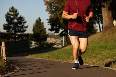 Photo of Athletic young man in sportswear running outdoors, closeup. Space for text
