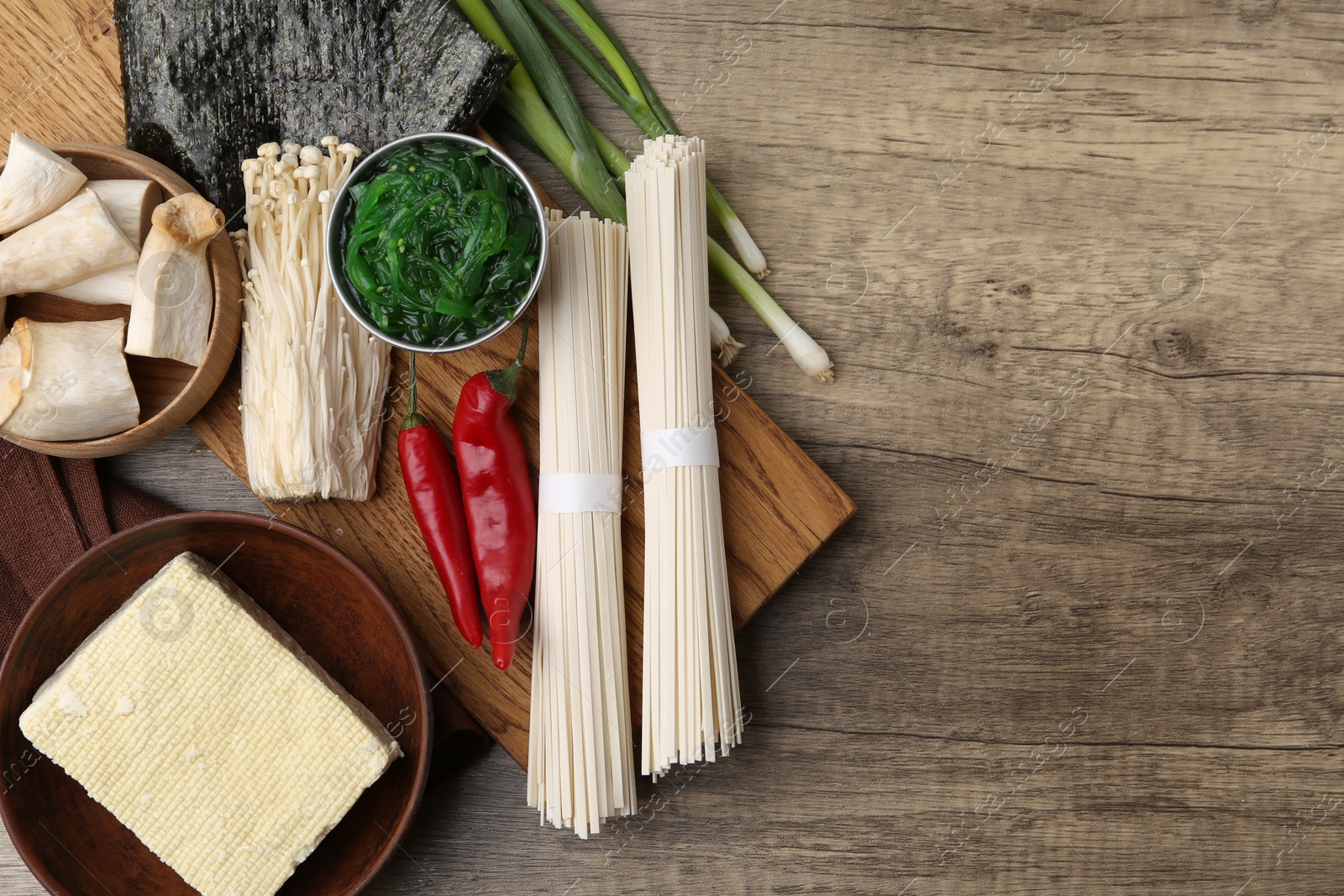 Photo of Enoki, king oyster (eryngii) mushrooms and other ingredients for ramen on wooden table, flat lay. Space for text