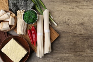 Photo of Enoki, king oyster (eryngii) mushrooms and other ingredients for ramen on wooden table, flat lay. Space for text