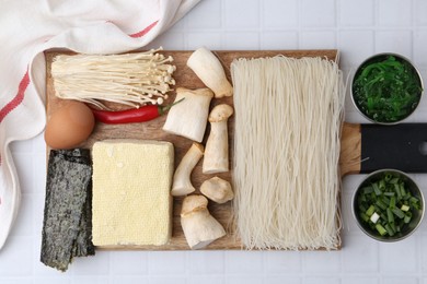 Photo of Enoki, king oyster (eryngii) mushrooms and other ingredients for ramen on white tiled table, flat lay
