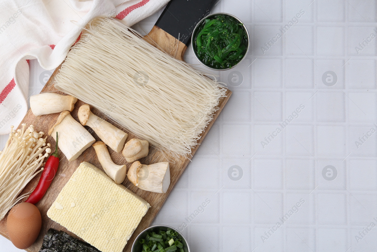 Photo of Enoki, king oyster (eryngii) mushrooms and other ingredients for ramen on white tiled table, flat lay. Space for text