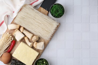 Photo of Enoki, king oyster (eryngii) mushrooms and other ingredients for ramen on white tiled table, flat lay. Space for text
