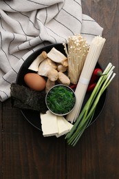 Photo of Enoki, king oyster (eryngii) mushrooms and other ingredients for ramen in bowl on wooden table, top view