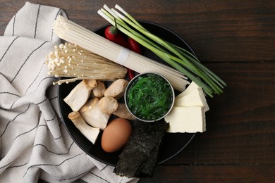 Photo of Enoki, king oyster (eryngii) mushrooms and other ingredients for ramen in bowl on wooden table, top view