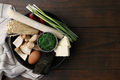 Photo of Enoki, king oyster (eryngii) mushrooms and other ingredients for ramen in bowl on wooden table, top view. Space for text