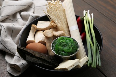 Photo of Enoki, king oyster (eryngii) mushrooms and other ingredients for ramen in bowl on wooden table, closeup