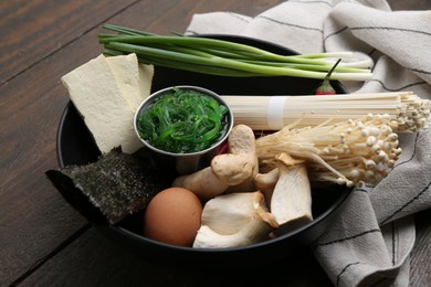 Photo of Enoki, king oyster (eryngii) mushrooms and other ingredients for ramen in bowl on wooden table, closeup