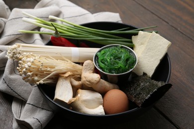 Photo of Enoki, king oyster (eryngii) mushrooms and other ingredients for ramen in bowl on wooden table, closeup