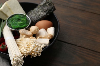 Photo of Enoki, king oyster (eryngii) mushrooms and other ingredients for ramen in bowl on wooden table, closeup
