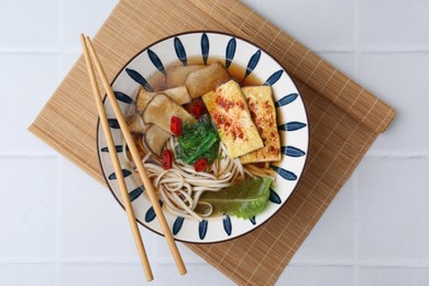 Photo of Tasty ramen with king oyster (eryngii) mushrooms in bowl on white tiled table, top view