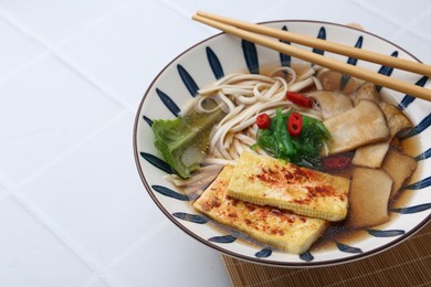 Photo of Tasty ramen with king oyster (eryngii) mushrooms in bowl on white tiled table, closeup