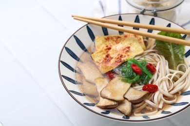 Photo of Tasty ramen with king oyster (eryngii) mushrooms in bowl on white tiled table, closeup