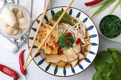 Photo of Tasty ramen with king oyster (eryngii) mushrooms in bowl and ingredients on table, flat lay