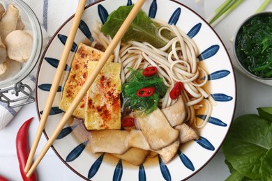 Photo of Tasty ramen with king oyster (eryngii) mushrooms in bowl and ingredients on table, flat lay