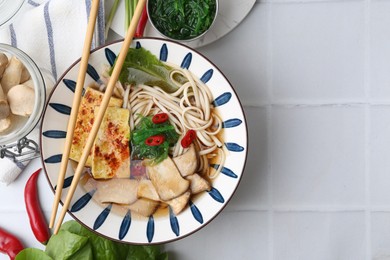 Photo of Tasty ramen with king oyster (eryngii) mushrooms in bowl on white tiled table, flat lay. Space for text