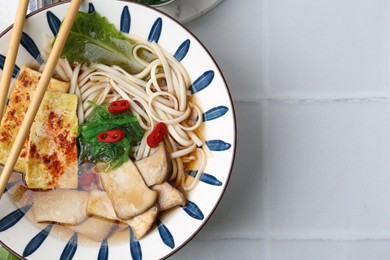 Photo of Tasty ramen with king oyster (eryngii) mushrooms in bowl on white tiled table, top view. Space for text