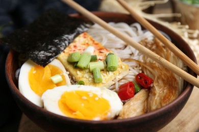 Photo of Tasty ramen with enoki mushrooms in bowl on table, closeup