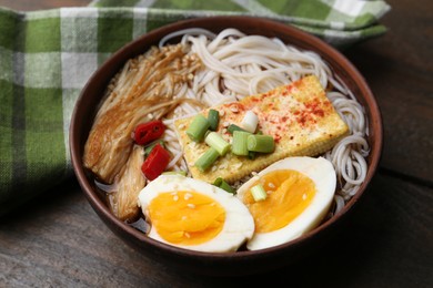 Photo of Tasty ramen with enoki mushrooms in bowl on wooden table, closeup