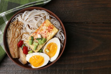 Photo of Tasty ramen with enoki mushrooms in bowl on wooden table, top view. Space for text
