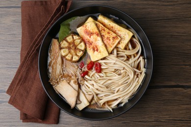 Photo of Tasty ramen with enoki and king oyster (eryngii) mushrooms in bowl on wooden table, top view
