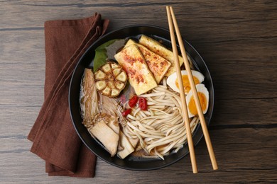 Photo of Tasty ramen with enoki and king oyster (eryngii) mushrooms in bowl on wooden table, top view