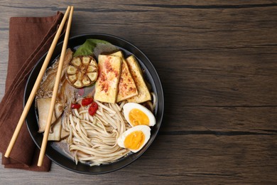 Photo of Tasty ramen with enoki and king oyster (eryngii) mushrooms in bowl on wooden table, top view. Space for text